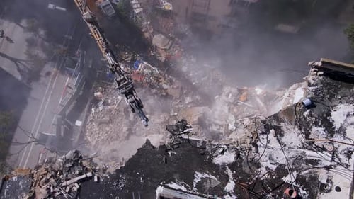 Vue aérienne d'une excavatrice en train de démolir un bâtiment, de la poussière s'élevant
