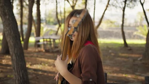 Young Woman Playing Guitar in Sunny Park