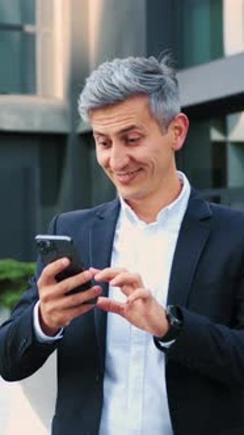 Excited Man Checks Phone Outside Modern Office Building