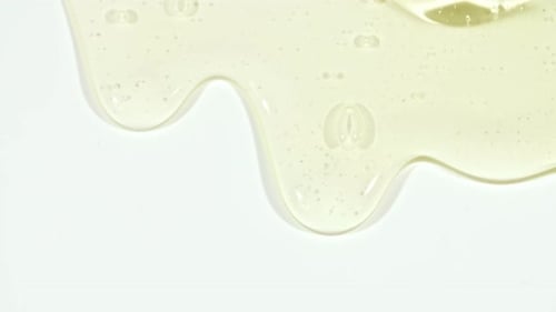 Yellow Transparent Cosmetic Gel Fluid With Molecule Bubbles Flowing On The Plain White Surface