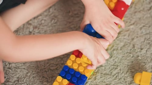 Kleine Hände, die helle Kunststoffkonstruktionen in Innenräumen herstellen. Kleine Kinder konzentrieren sich darauf, lebendige Strukturen zusammenzubauen