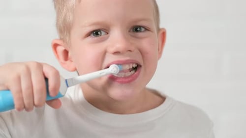 Child Brushing Teeth With Electric Toothbrush in Bathroom