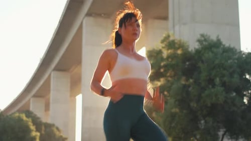 Sporty Woman Jogger Running Under Bridge During Sunny Day at City Park