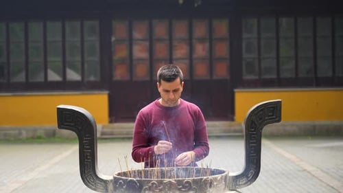 European man placing a burning incense stick in a Chinese temple. Slow motion