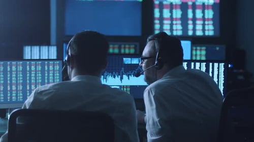 Team of stockbrokers are having a discussion in a dark office with display screens.