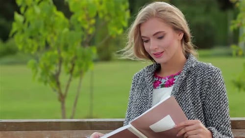 Woman Sitting on Bench Reads Notebook