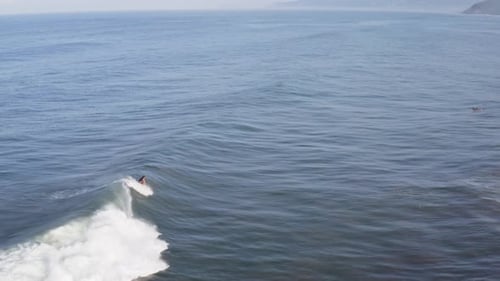 Aerial: surfer catching long beautiful wave and surf riding to beach, follow view