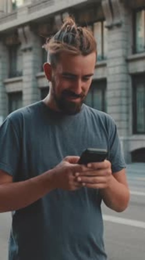 Young smiling man with beard stands on street using cellphone