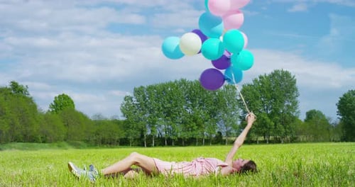 Woman Lying in Field Holding Colorful Balloons
