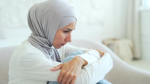 Woman in Hijab Sits with Knees Hugged in Sorrow