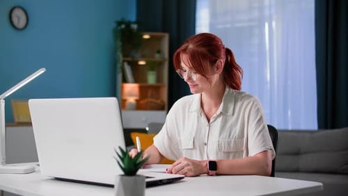 Remote Work Young Woman Works at Home at a Computer Makes Notes in a Notebook While Sitting at a