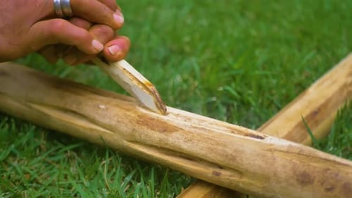 An individual is attempting to ignite a fire with a large piece of wood resting on the grass, utiliz