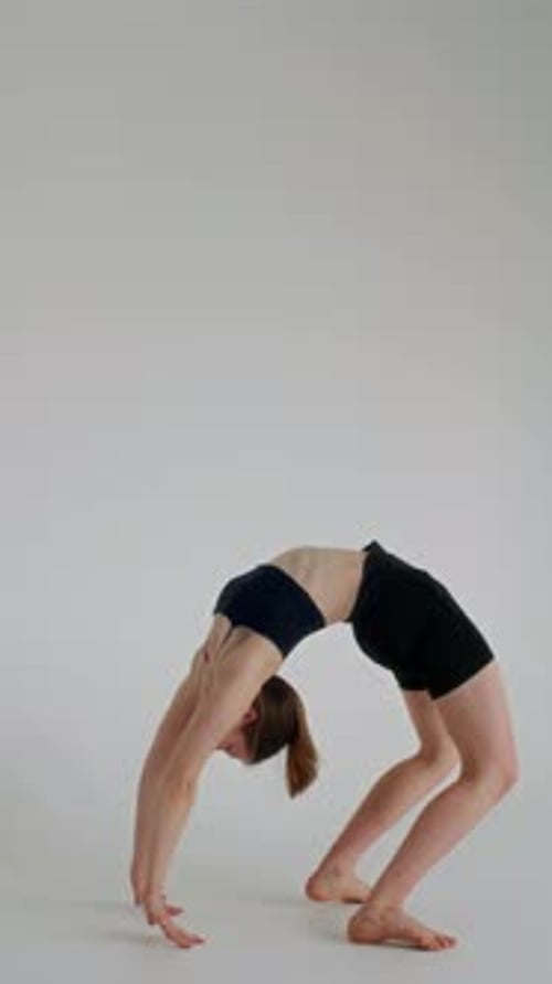 Fille pratiquant la pose d'une roue unijambiste dans un studio de yoga blanc