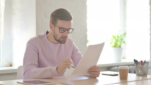 Young Man Upset While Reading Documents in Office