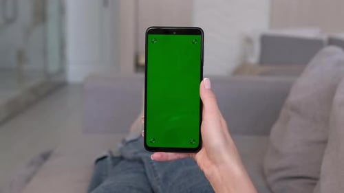 Woman Makes Swipe Up Gesture on Green Screen of Smartphone While Lying on Sofa at Home