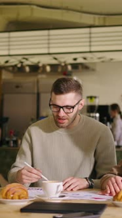Young Professionals Collaborating at Cafe Table with Documents Coffee and Pastries Focusing on