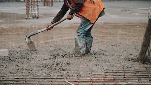 Arbeiter nivelliert nassen Beton manuell mit einer Schaufel