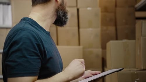 Un bel employé d'entrepôt utilise une tablette numérique pour vérifier les stocks