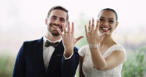 Imágenes de vídeo en 4K de una cariñosa joven pareja de recién casados mostrando sus anillos de boda al aire libre