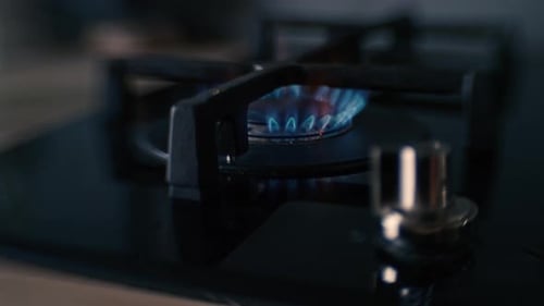 A distorted shot of a black ceramic gas stove hob being lit, the fire burns for a while, and is then