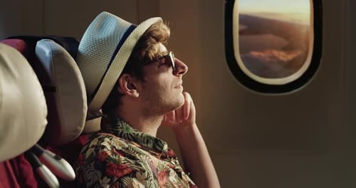 Cinematic shot of young man wearing straw hat and sunglasses sitting in cabin of aircraft and enjo
