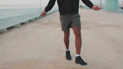 Young athlete jumping rope on the embankment. Camera moves upwards