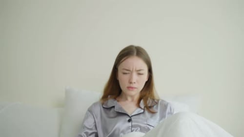 Une
belle fille malade caucasienne en pyjama se lève du sommeil dans la chambre.