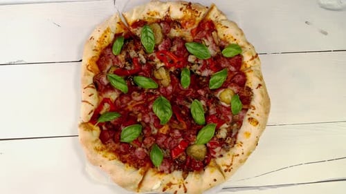 Geschnittene ganze Pizza mit Fleisch, Wurst, Pfeffer, gesalzene Gurke, Basilikum