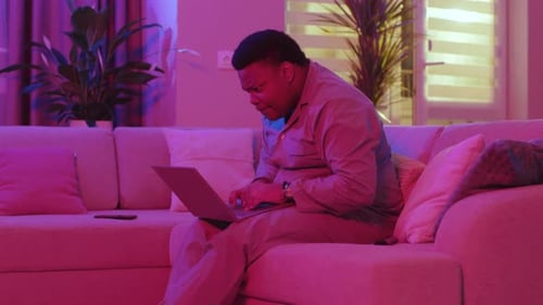Man Works on Laptop Sitting on Couch at Home