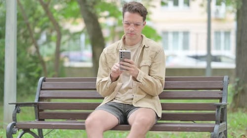 Man Using Smartphone Sitting on Park Bench
