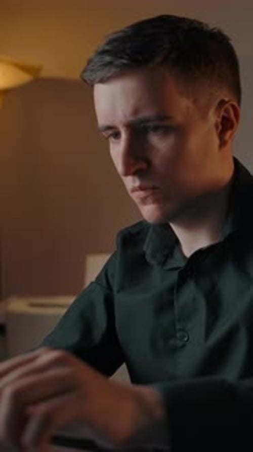 Vertical of A Young Man Works on a Laptop Typing on a Keyboard