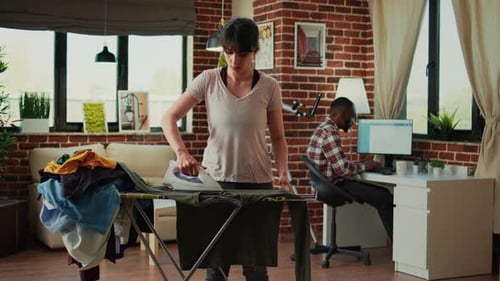 Woman Ironing Clothes While Man Works at Home