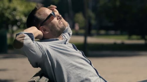 Young man enjoys sunshine and relaxation on a bench in the city park