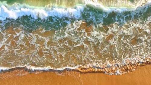 White foamy waves come to the shore. Sunny coast of the Pacific Ocean from aerial perspective.