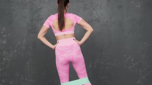 Fitness girl doing workout on legs and buttocks. Brings back the right leg. Back view. A young woman