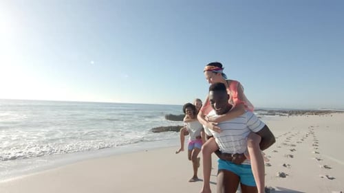 Young African American man gives a piggyback ride to a young Caucasian woman on the beach