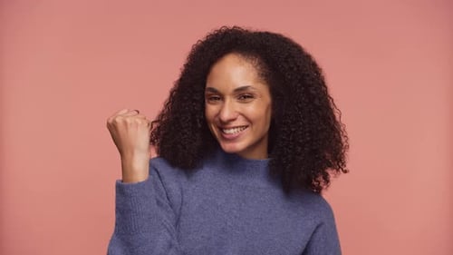 Excited Woman Celebrating Victory with Fist Pump on Pink Background