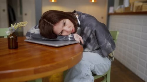 A Tired Brunette Girl in a Gray Sweater a Cafe Visitor Lies on a Laptop at the Table and Sleeps in a