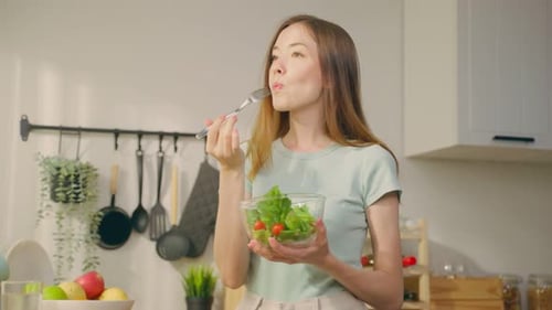 Portrait of young Caucasian girl eating green salad in kitchen at home.