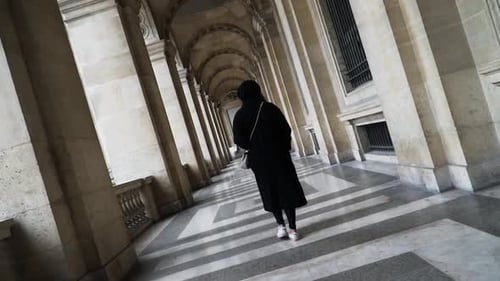 Uma mulher andando no corredor em arco no pátio do Museu do Louvre, Paris, França. Rotati