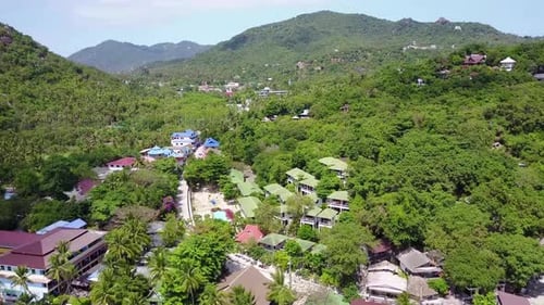 Aerial view at tropical island. Camera moves forward from coastline deep into the island. Bright sun