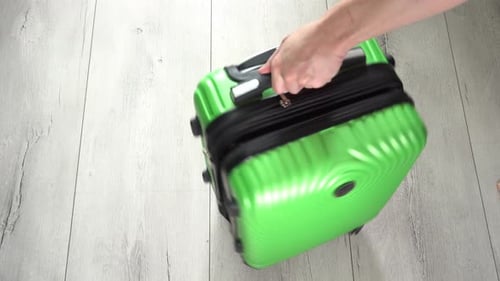 Guy rotate the green baggage case with clothes in hand luggage. Tourist pack things for a trip