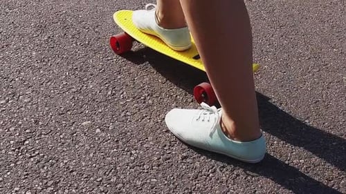 Teenage girl feet riding modern cruiser skateboard on urban road in slow motion
