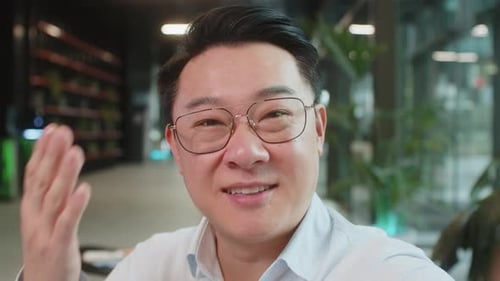 Portrait of Happy Chinese Businessman Looking at Camera and Waves Hand Hello in Office Hotel Lobby