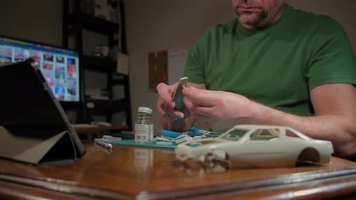 Homme assembleur modèle en plastique de voiture dans une pièce à table selon les dessins et les instructions, plan large