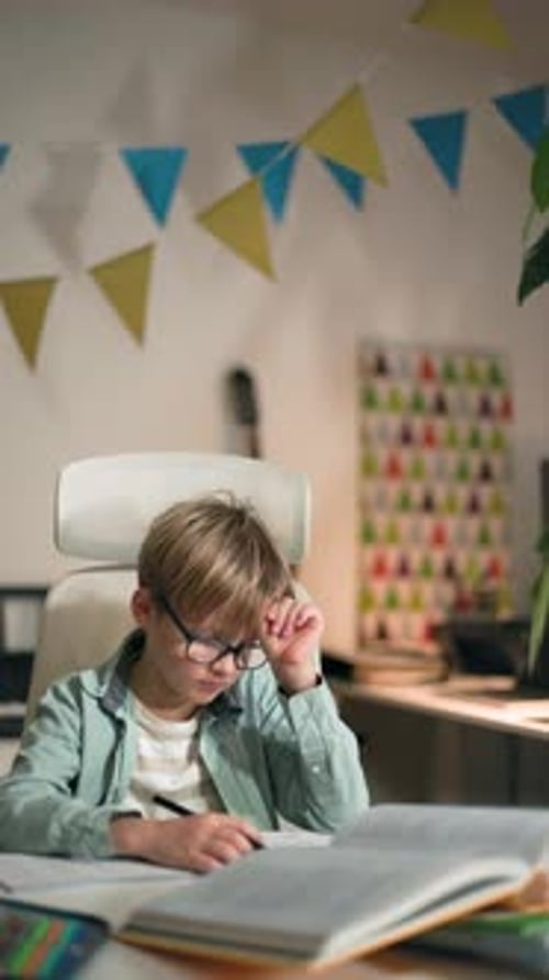 Schoolboy in Glasses Sitting at the Table Has Grown Tired of Doing His Homework