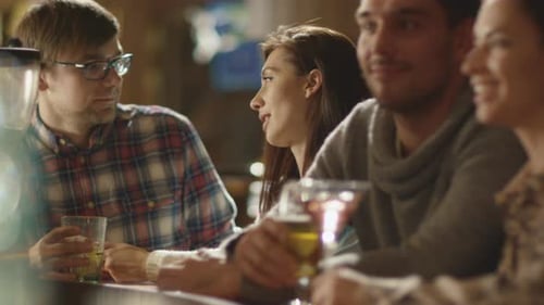 Friends laugh, drink beer and cocktails while having a good time together at a bar.