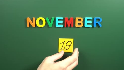 Hand sticking a sticker 19 November calendar day on school board. 19 date of November. Nineteenth