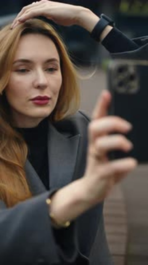 Businesswoman styling hair and taking selfie with smartphone on modern outdoor terrace