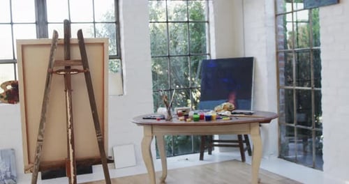 Close up of canvas on easel and paints and brushes on table in studio, slow motion